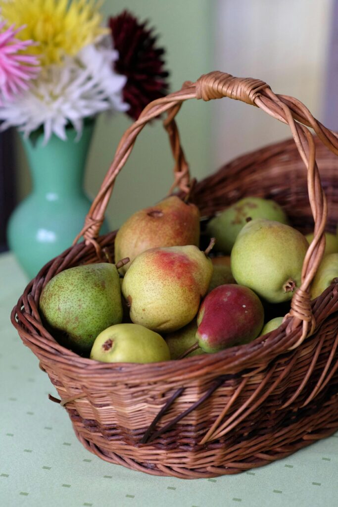 pexels-photo-34062813-34062813 Vibrant pears in a wicker basket with flowers in the background, perfect for kitchen decor.