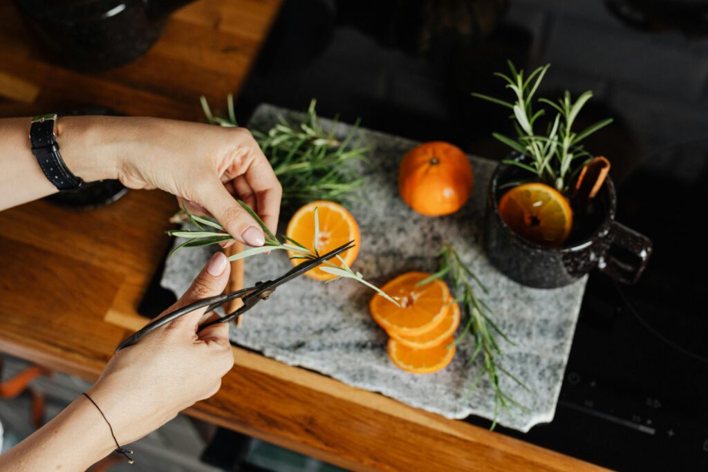 pexels-photo-5421520-5421520 A close-up of hands cutting fresh rosemary next to sliced oranges on a kitchen countertop, ideal for culinary themes.