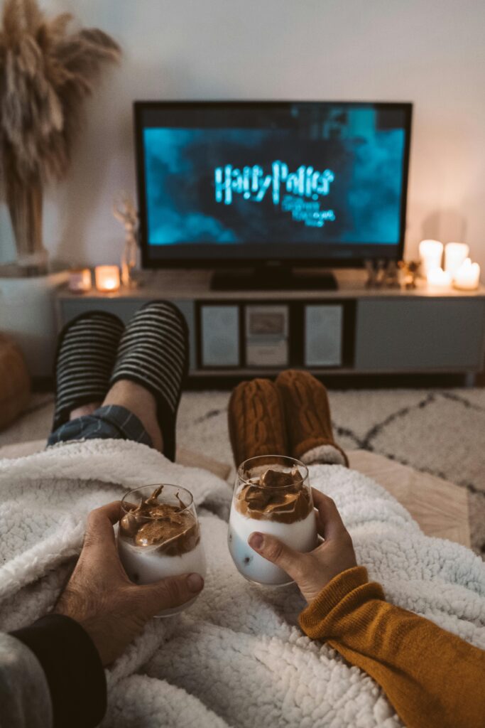 pexels-photo-4488194-4488194 A couple enjoys a cozy movie night with drinks, wrapped in blankets, watching a Harry Potter film on TV.
