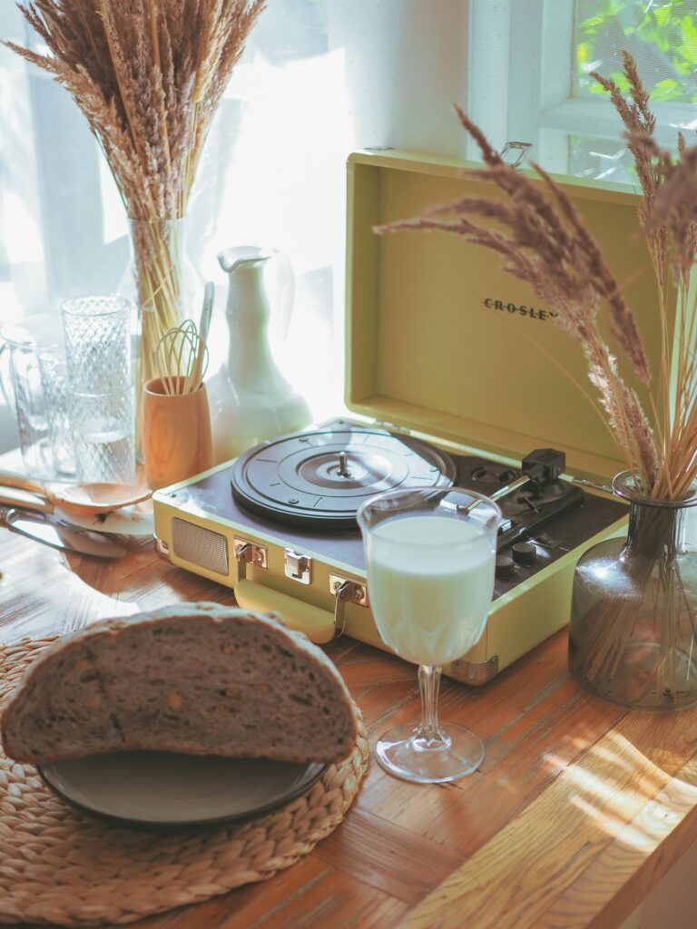 pexels-photo-9298565-9298565 A cozy vintage still life arrangement with a turntable, bread, and milk by a sunlit window.
