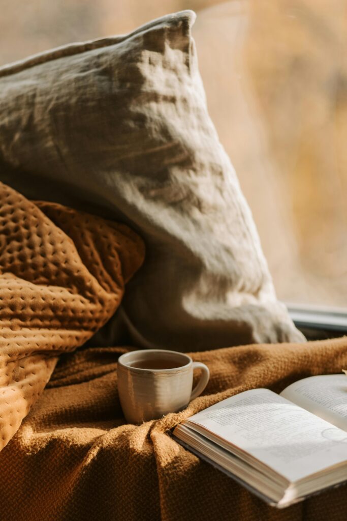 pexels-photo-9969204-9969204 Warm and inviting interior scene with cozy fall essentialsfeaturing a cozy mug and open book on a blanket.