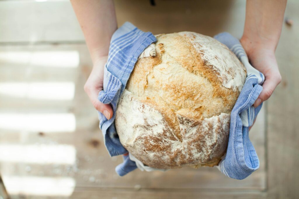 pexels-photo-263168-263168 Close-up of artisan bread held in hands with a blue cloth on a wooden table.