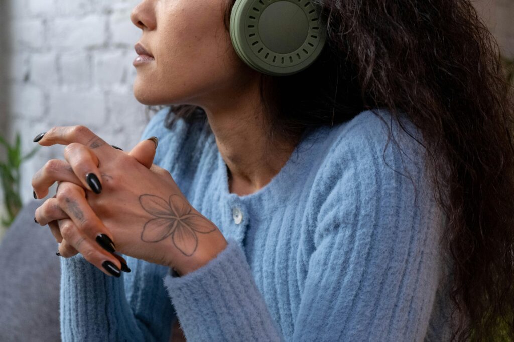 pexels-photo-6686434-6686434 Close-up of a woman listening to music with headphones, wearing a blue sweater and showcasing a floral tattoo on her hand.